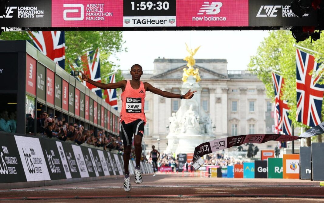 Sebastian Sawe cruzando la meta de la Maratón de Londres 2026 con el cronómetro marcando 1h59m30s